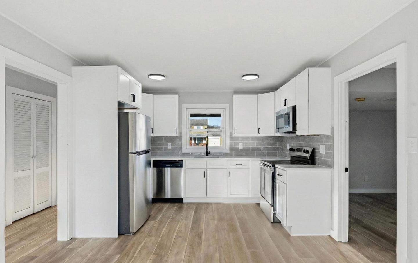 Renovated kitchen with white cabinets, tile backsplash and plank flooring